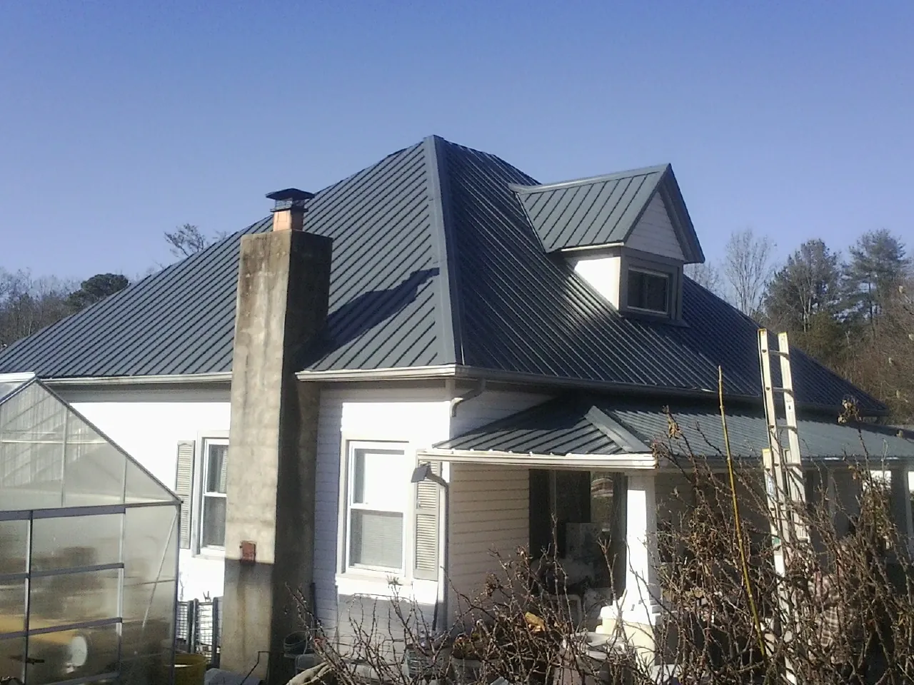Dark blue standing seam metal roof on a white farmhouse with dormer — Slate & Tile Roof Repair by Roofing Brothers in Knowlesville