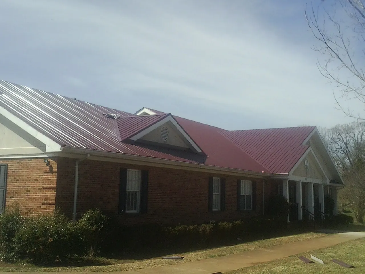 Red metal roof with gabled entries on a long brick building, from a Hail Damage Roof Repair job in Knowlesville