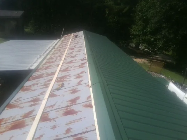 Old rusted panels beside newly installed green metal roofing — Wind Damage Roof Repair by Roofing Brothers in Knowlesville