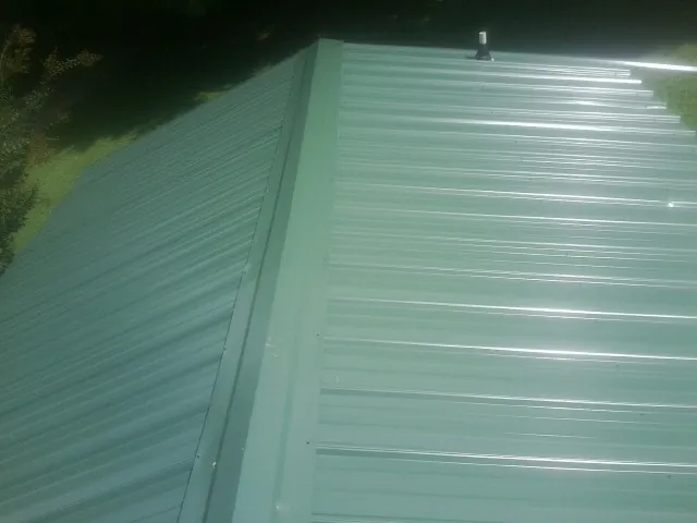 New green metal panels meeting at the ridge of a roof — Flat Roof Repair work by our crew in Knowlesville