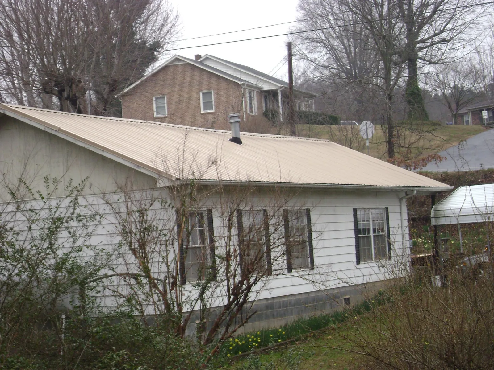 Tan metal roof on a white sided house set into a hillside — Commercial Roofing by Roofing Brothers in Knowlesville