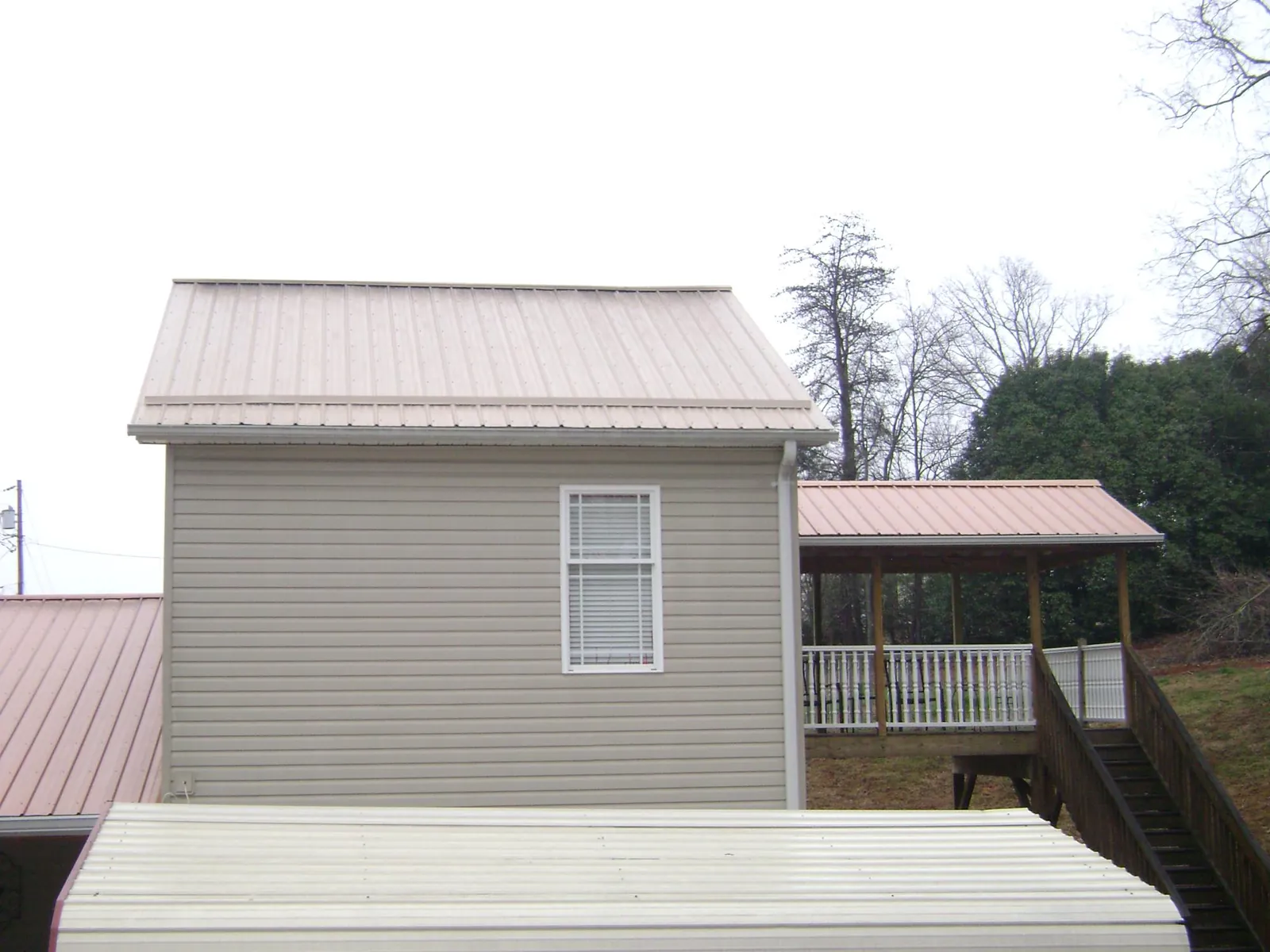 Tan metal roofs on a two story addition and attached porch, from a Roof Replacement job in Knowlesville